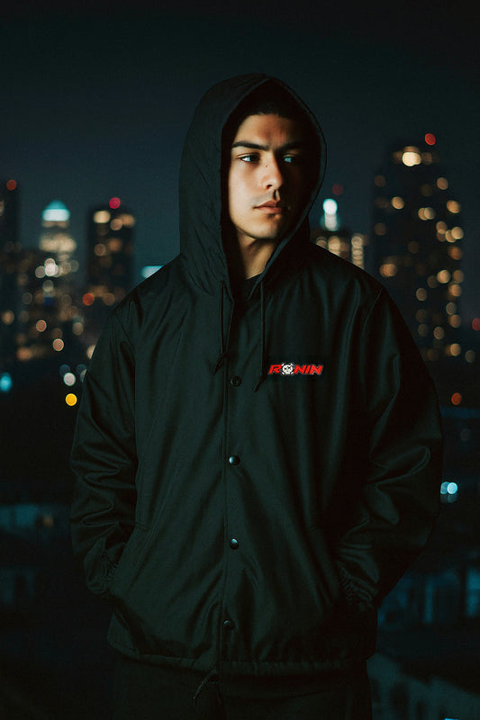 Person wearing a black hoodie with a logo against a cityscape at night