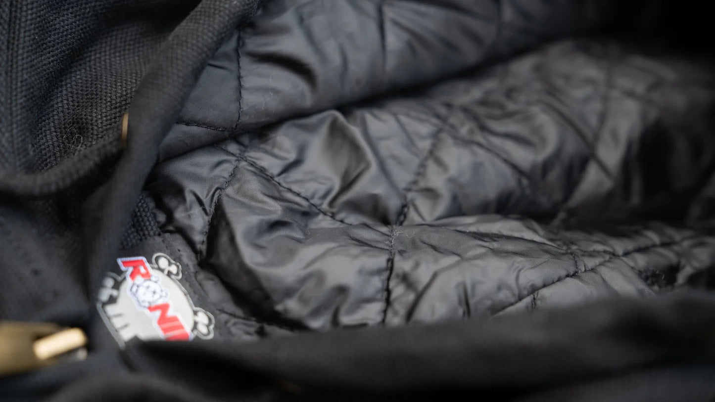 Close-up of a black quilted jacket with a brand logo on a dark background