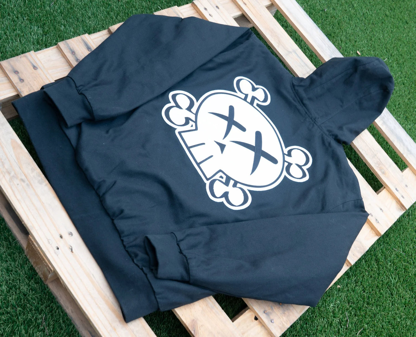 Black hoodie with a white graphic skull logo design on a wooden pallet