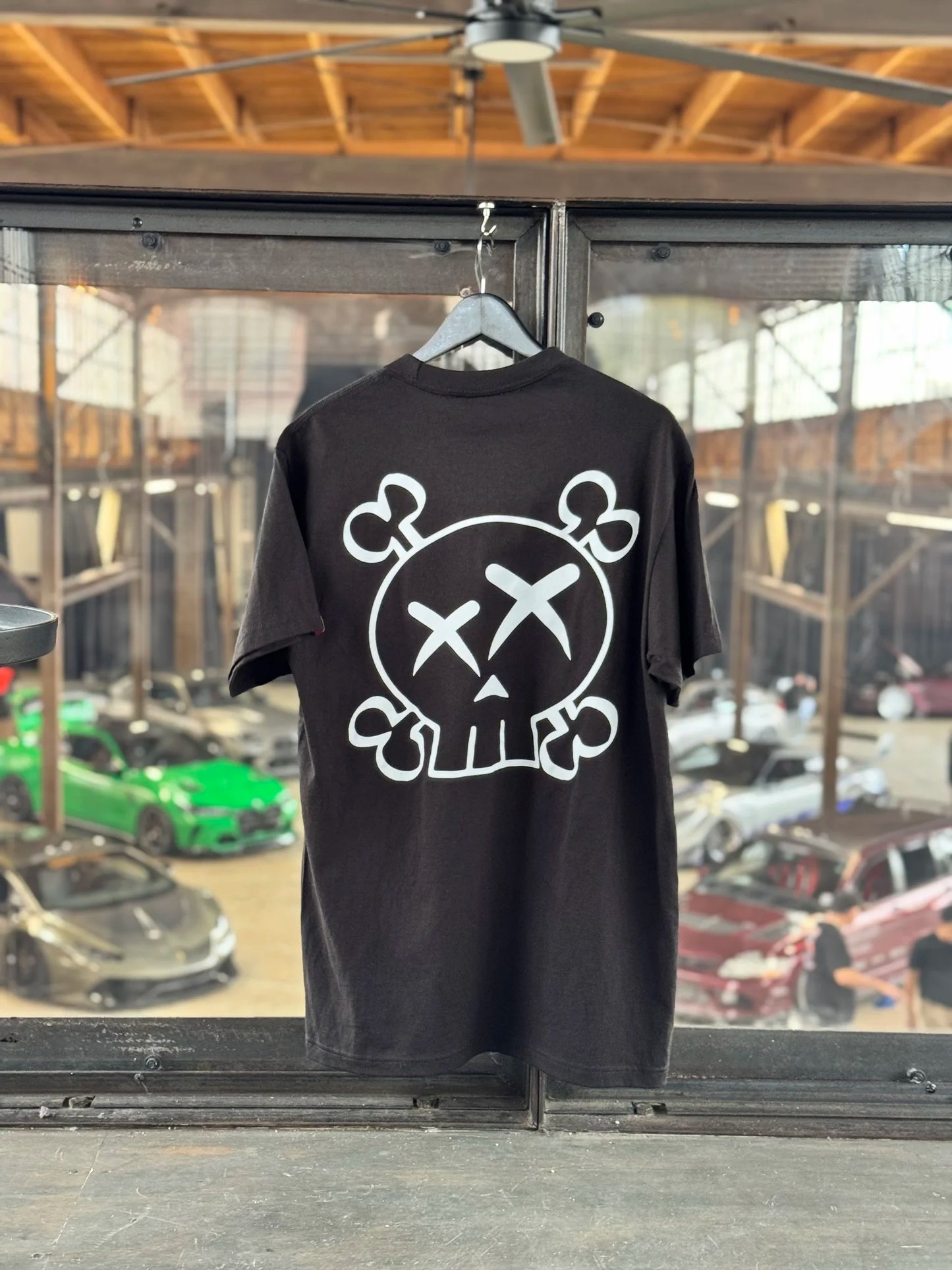 Black t-shirt with a white graphic design on a hanger in front of a window view.