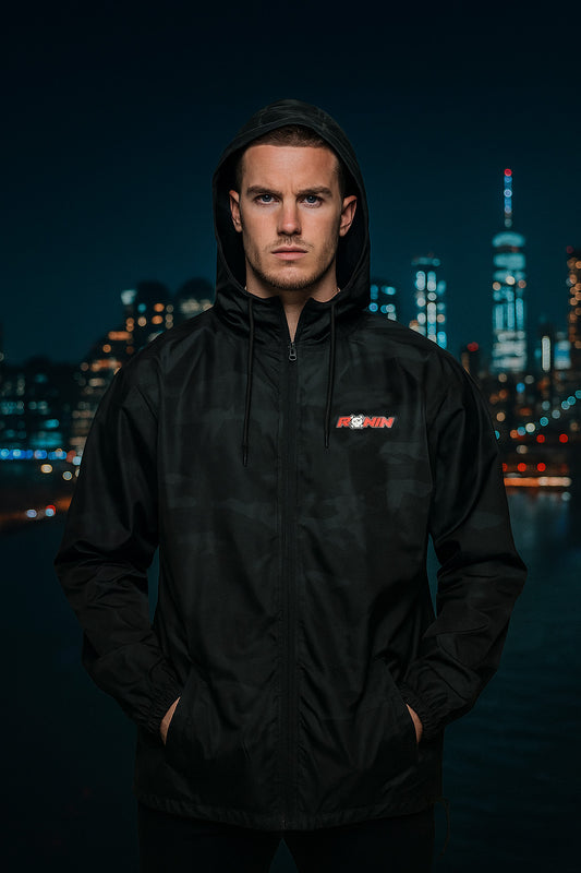Person wearing a black camo jacket with a logo against a city skyline at night