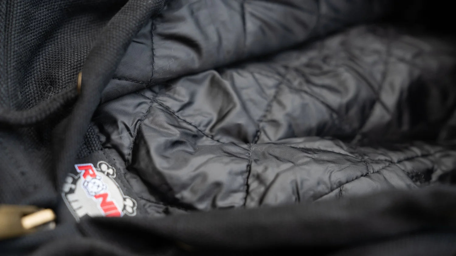 Close-up of a black quilted jacket with a brand logo on a dark background