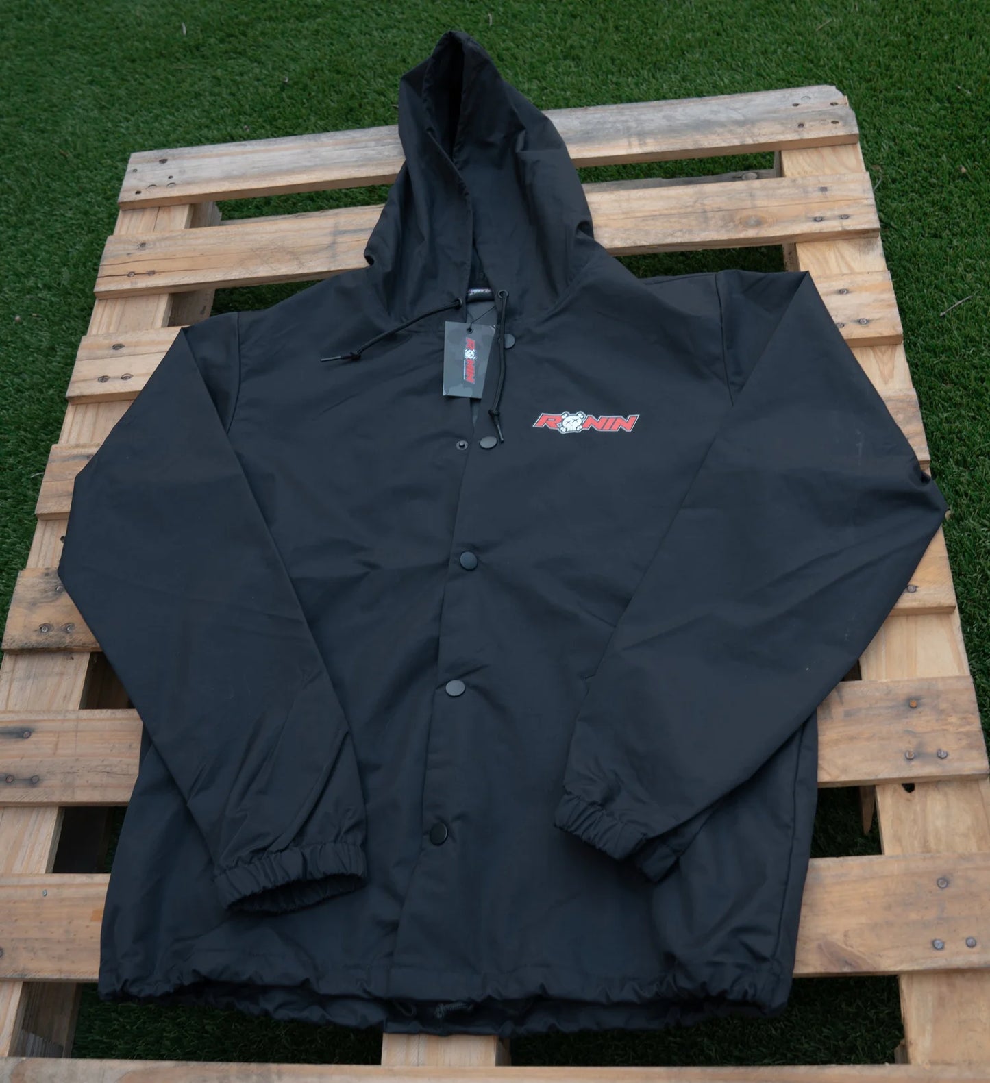 Black jacket with a brand logo on a wooden pallet against a grassy background
