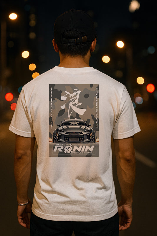 Person wearing a white t-shirt with a Nissan GTR graphic design on the back, standing against a blurred street background.