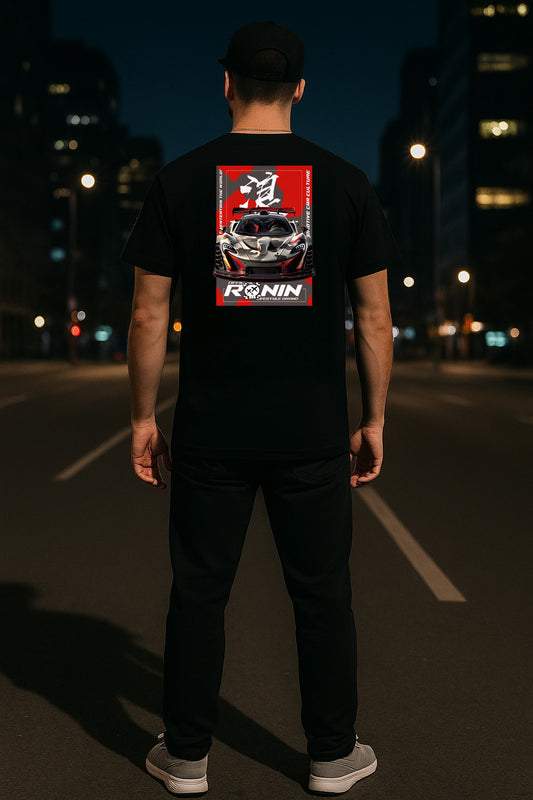 Person wearing a black t-shirt with a McLaren P1 graphic design on the back, standing on a street at night.