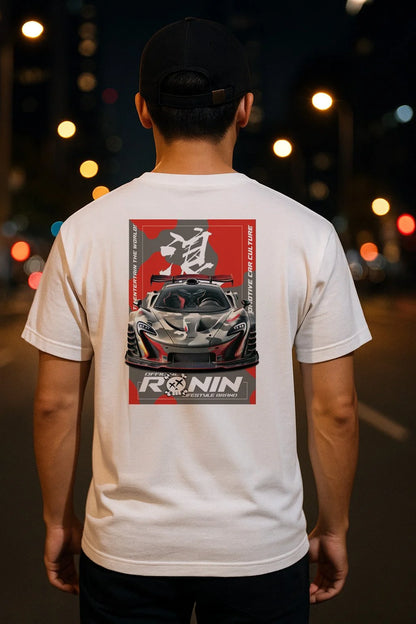 Person wearing a white t-shirt with a graphic design of a McLaren P1 on the back, standing on a street at night.