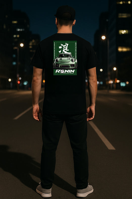 Person wearing a black t-shirt with a green Porsche GT3RS and white graphic on the back, standing on a dark street at night.